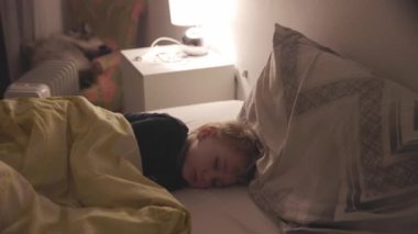 Sevimli küçük çocuk lambanın ışığında büyük bir yatakta uyuyor. Orta çekim