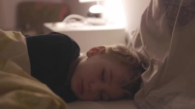 Sarışın küçük çocuk bir lambanın ışığında uyuyor. Orta çekim