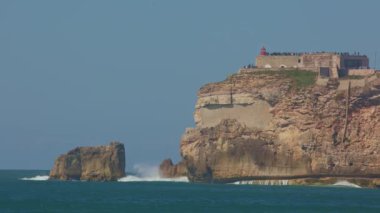 Deniz dalgaları kayalara çarpıyor. Gözlem güvertesi uçurumun tepesinde. Orta çekim