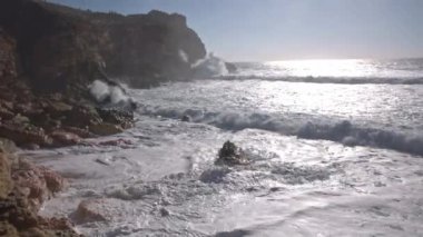 Deniz dalgaları kayalara çarpar ve kıyıları ağır çekimde kaplar. Orta çekim