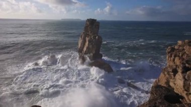 Gün ışığında deniz dalgaları kayalık bir uçuruma çarpar. Orta çekim