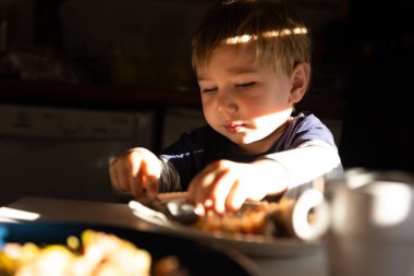 Bir Küçük Çocuk Masa 'da Yemek yer, güneş ışığı yüzüne vurur. Orta çekim