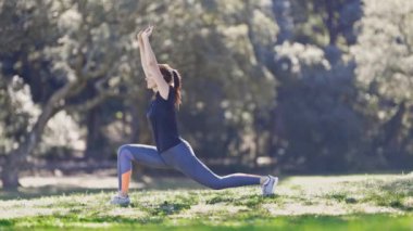 Gözlüklü spor kadını doğada esneme hareketleri yapıyor. Orta çekim