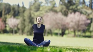 Gözlüklü gülümseyen yetişkin kadın, elleri arkada lotus pozisyonunda oturur. Orta çekim