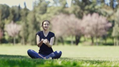 Gözlüklü gülümseyen yetişkin kadın lotus pozisyonunda oturur ve ellerini uzatır. Orta çekim