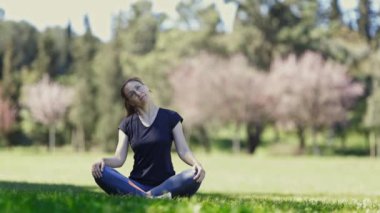 Gözlüklü gülümseyen yetişkin kadın lotus pozisyonunda oturur ve boynunu ısıtır. Orta çekim