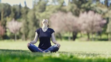 Gözlüklü yetişkin bir kadın lotus pozisyonunda oturur ve boynunu ısıtır. Orta çekim