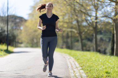Yetişkin gülümseyen fitness kadını parkta koşuyor. Orta çekim