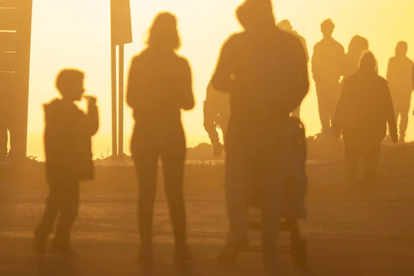 Silhouettes of people in the light of a bright orange sunset. Mid shot