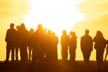 Parlak sarı bir günbatımında tepede duran insanların siluetleri. Orta çekim