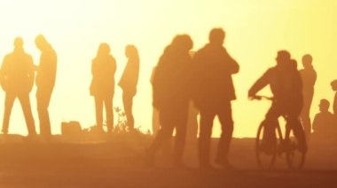 Gün batımında siluet halindeki insanlar - insanlar bisiklet ve scooterlara biniyor. Orta çekim