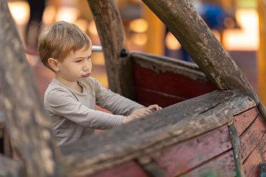 Oyun parkındaki tahta teknede oturan komik bir çocuk. Orta çekim