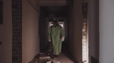 Koruyucu kıyafetli ve gaz maskeli bir adam terk edilmiş binanın koridorunda yürüyor. Orta çekim
