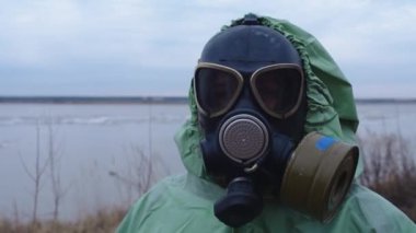 Kıyamet sonrası konsept - gaz maskeli bir adam bulutlu bir manzaranın arka planında koruyucu elbise giyiyor. Portre