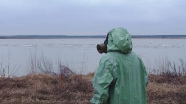 Kıyameti andıran bir kavram. Gaz maskeli, koruyucu takım elbiseli bir adam bulutlu manzaranın arka planına bakıyor. Orta çekim