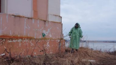 Kıyamet sonrası konsepti: Gaz maskeli, koruyucu takım elbiseli bir adam terk edilmiş bir binanın etrafında dolaşıyor. Orta çekim