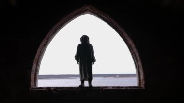 Koruyucu takım elbiseli ve gaz maskeli bir adam terk edilmiş bir binanın kemerinde duruyor. Orta çekim