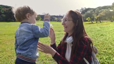 Küçük oğluyla yeşil bir tarlada oturan karahindiba ile oynayan tatlı bir anne. Orta çekim