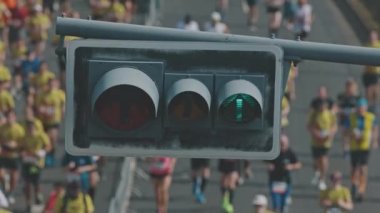 Ön planda trafik ışığı var. İnsanlar köprüde yarım maraton koşuyor. Orta çekim
