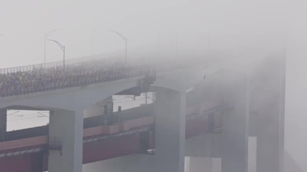 橋の上でハーフマラソンを走る人々 人々は厚い霧の中を走っています ミッドショット — ストック動画