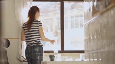 Yetişkin bir kadın mutfaktaki bir pencereye cam sileceği sıkar. Orta çekim