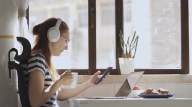 Kulaklıklı bir iş kadını mutfakta telefonuyla çalışıyor. Orta çekim