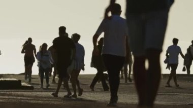 19 Nisan 2023 Lizbon, Portekiz: Costa da Caparica - deniz kenarında yürüyen yaz elbiseli turist siluetleri. Orta çekim