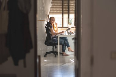 Mutfak masasında çalışan serbest çalışan gülümseyen kadın kameraya bakıyor. Orta çekim