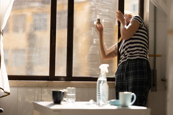 stock image Adult woman housewife washing the outside of a window in the kitchen. Mid shot