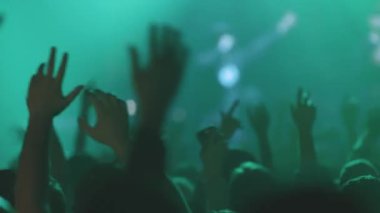 Kalabalıktaki insanlar canlı bir konserde kollarını yanlara sallıyorlar. Orta çekim