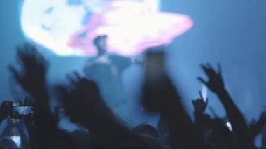 Kalabalıktaki insanlar canlı bir rap konserinde kollarını yana doğru sallıyorlar. Orta çekim