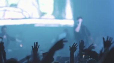 Kalabalıktaki insanlar canlı bir rap konserinde ellerini yana doğru sallıyorlar. Orta çekim