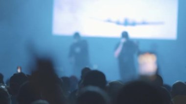 Sahnede rap yapan sanatçı ve insanlar şovu telefonlarıyla çekiyorlar. Orta çekim