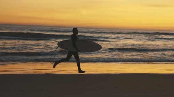 Gün Batımında Sörf Tahtasıyla Deniz Kıyısında Koşan Atletik Bir Adam — Stok video