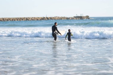 Sörfçü bir aile. Dalgıç elbiseli bir baba ve oğul denize açılır. Orta çekim