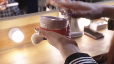 Kuliste makyaj yapan genç bir kadın şapkadaki tozu silkeliyor. Orta çekim