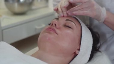 Bir kozmetologla seans. Terapist ameliyattan sonra kadın müşterinin yüzünü siliyor. Orta çekim