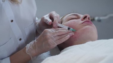 Kozmetik uzmanının randevusunda derisi sorunlu bir kadın yanağına enjeksiyon yapar. Orta çekim