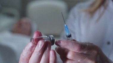 Bir sağlık çalışanı şişeden şırıngaya bir çözüm çizer. Orta çekim