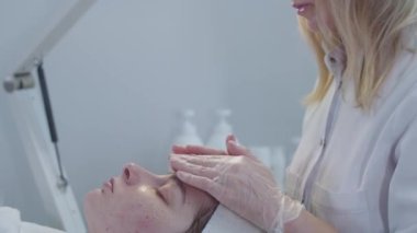 Kozmetik tedavisi. Kadın üstat ameliyattan sonra müşterisinin yüzüne yumuşak bir masaj yapıyor. Orta çekim