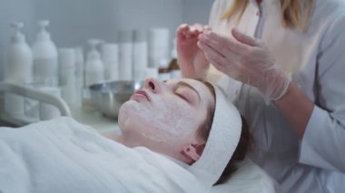 Kozmetik tedavisi, kadın müşterinin yüzündeki maskenin kalıntılarını çıkarmak. Orta çekim
