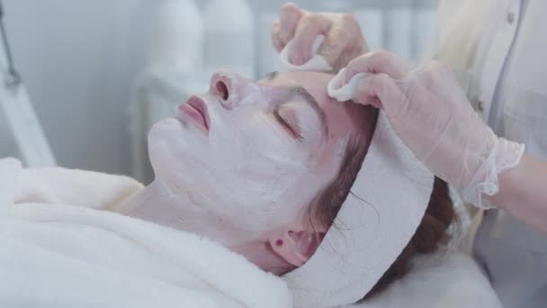 Αισθητικός Σκουπίζει Δέρμα Των Πελατών Από Λευκή Μάσκα Μεσαίο Πλάνο — Αρχείο Βίντεο