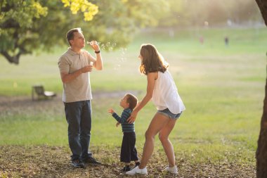 Mutlu beyaz aile parkta vakit geçiriyor. Babası sabun köpüğü üflüyor. Orta çekim