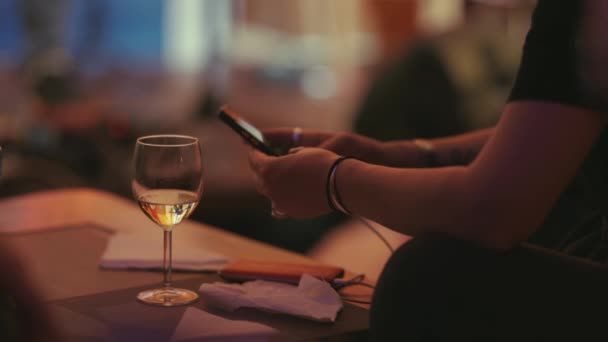 一个人坐在吧台旁 用他的电话 旁边站着一杯葡萄酒 — 图库视频影像