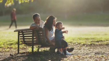 Bir bankta oturan ebeveynler oğullarının sabun köpüğüyle oynamaları. Orta çekim