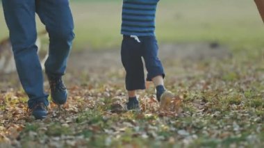 Küçük bir çocuk, ailesi onları elleriyle tutarken parkta yürüyor. Orta çekim