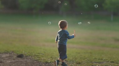 Parkta sabun köpüğü kovalayan küçük bir çocuk. Orta çekim