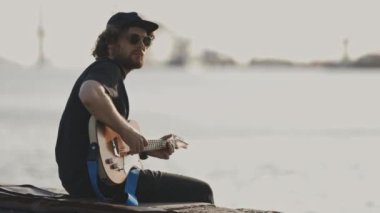 Soğuk adam rıhtımda gitar çalıyor. Orta çekim