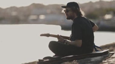 Rıhtımda gitar çalan bir hippi. Orta çekim