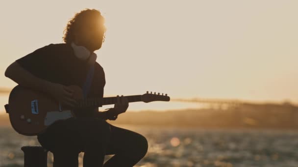 Ein Mann Der Draußen Bei Hellem Sonnenuntergang Wasser Gitarre Spielt — Stockvideo